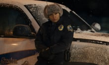 A detective leans on her car in the snow.