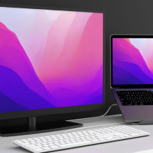 Laptop on stand next to desktop monitor, keyboard, and coffee mug
