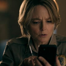 A police officer wearing headphones stares at a smartphone with concentration.
