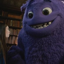 A large, fluffy, purple creature smiles at a young girl.