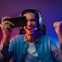 Happy asia man gamer wear headphone competition play video game online with smartphone colorful neon light in living room at night modern house. Esport streaming game online, Home quarantine activity.
